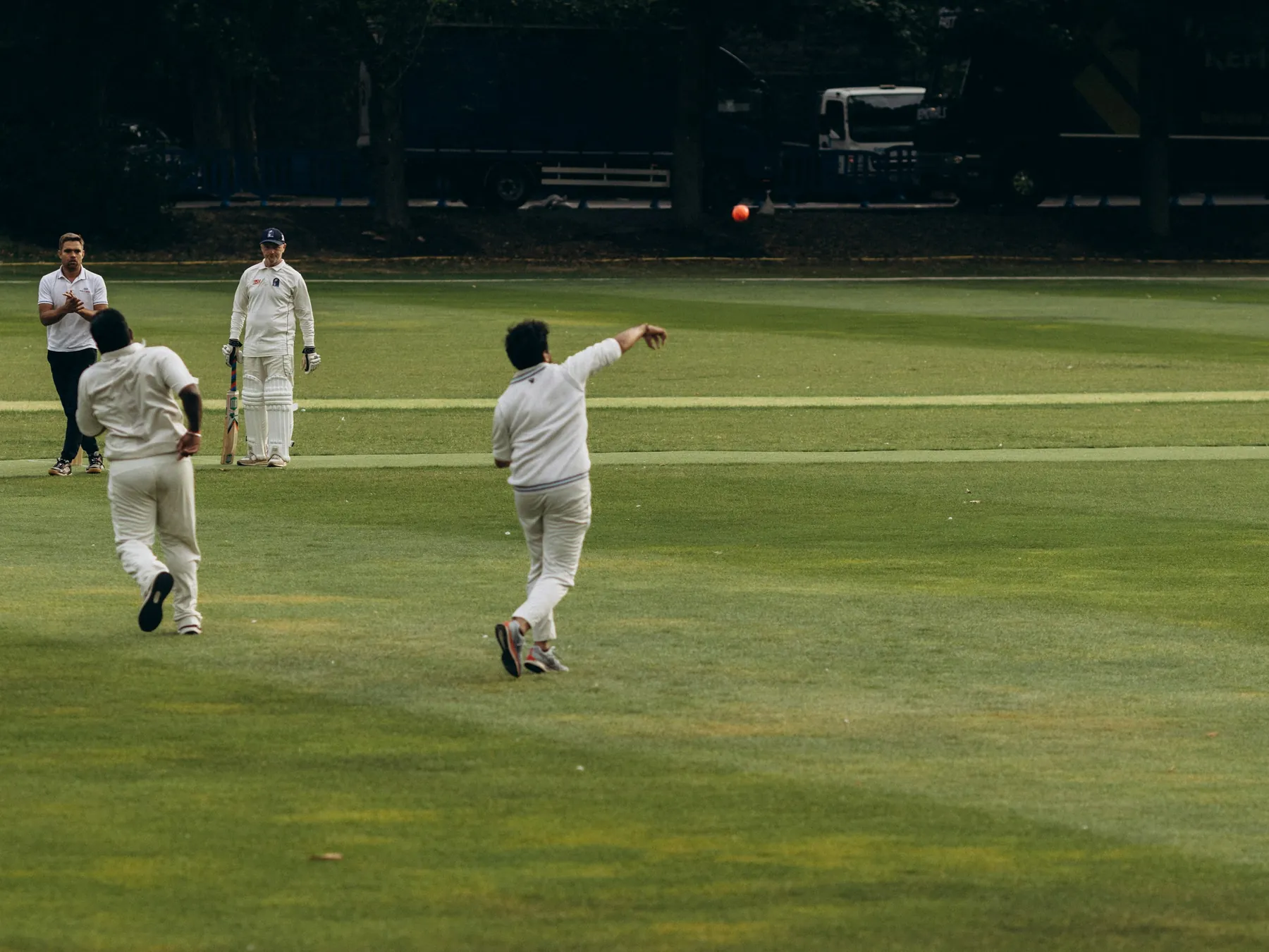 Cricket bowler delivering a red ball on the pitch