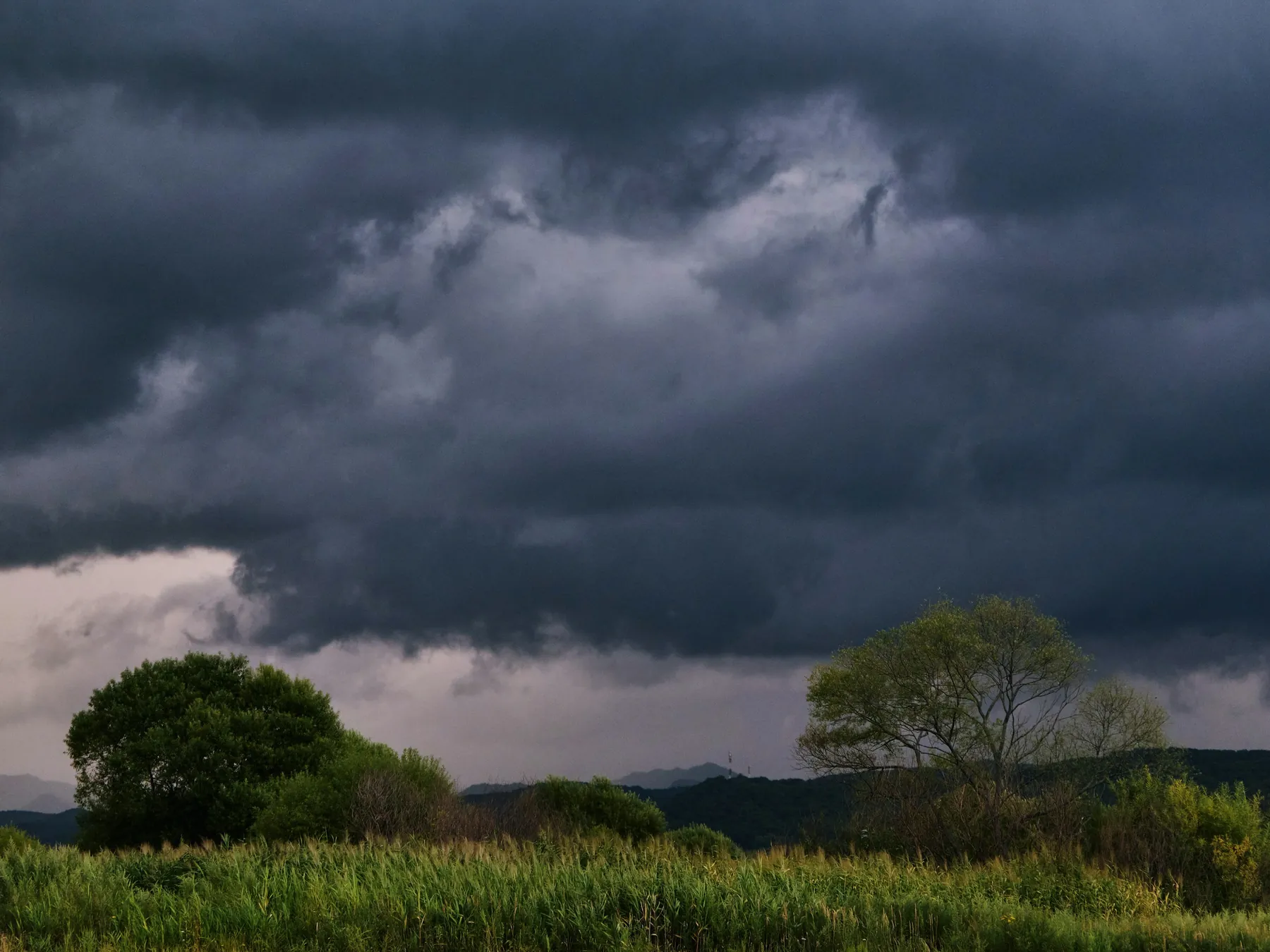 Dark layered storm clouds gathering above a green rural field