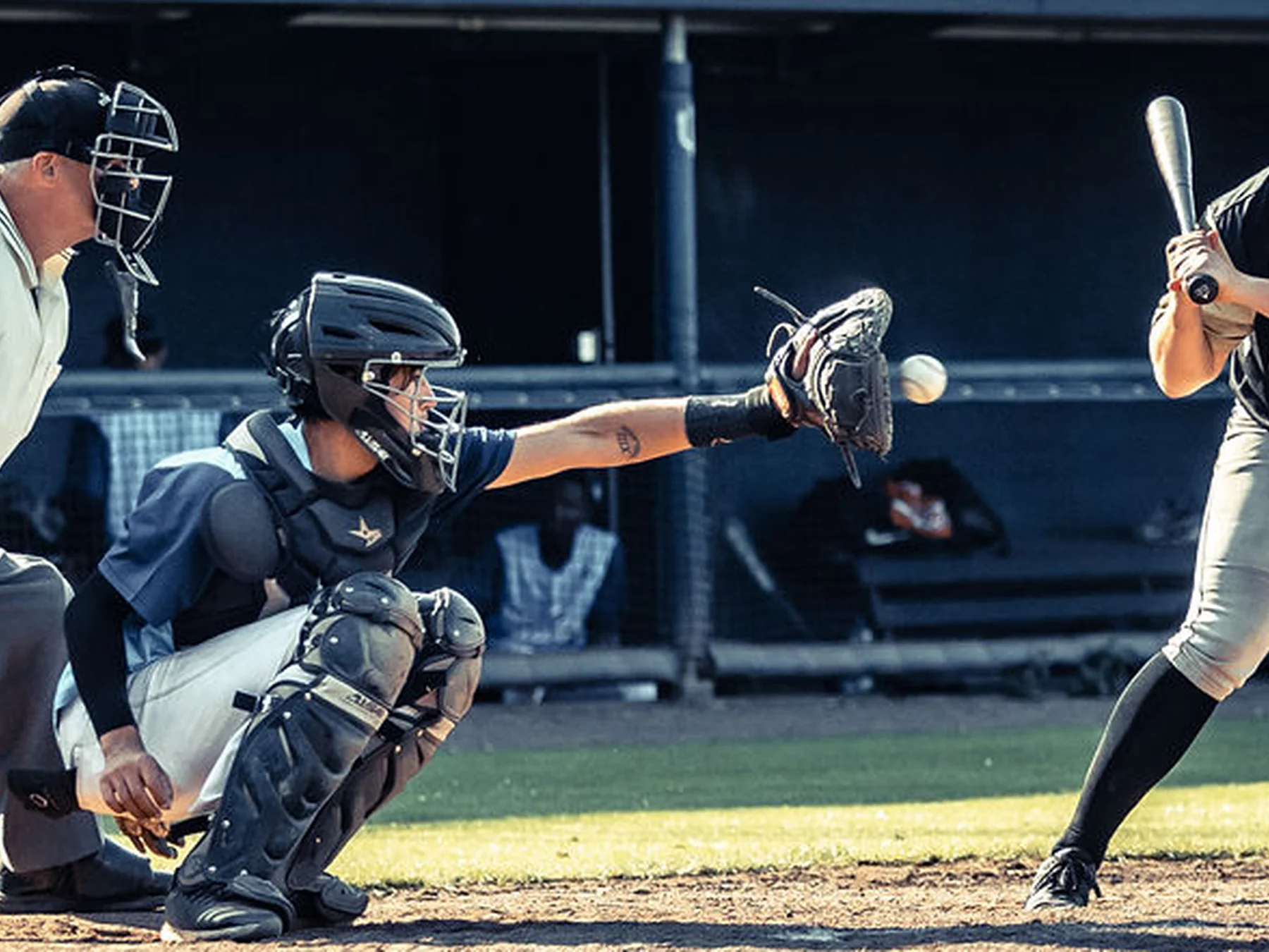 Baseball catcher reaching for a pitch with the batter and umpire nearby