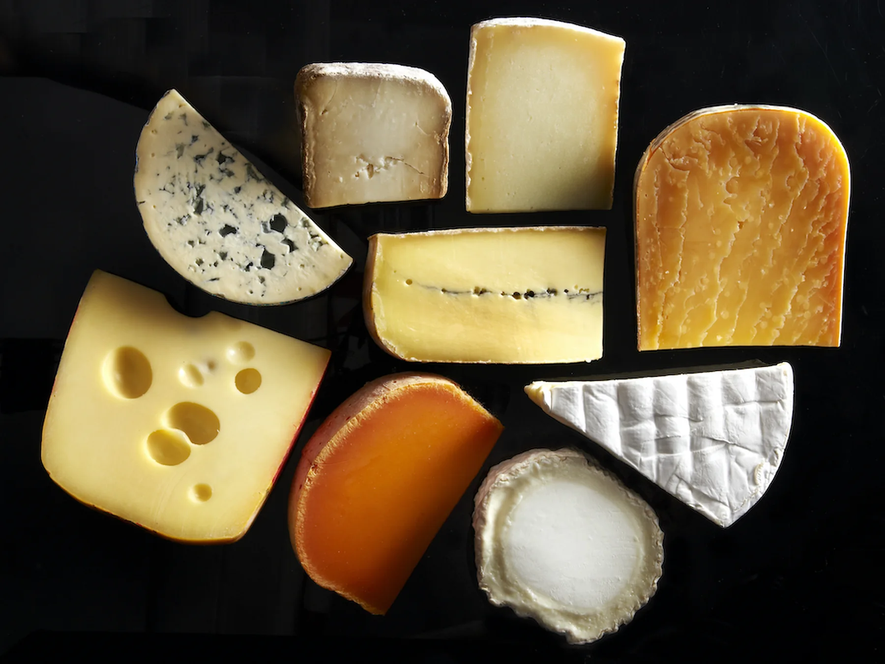 Assortment of blue, soft, hard, and holey cheeses on a dark background