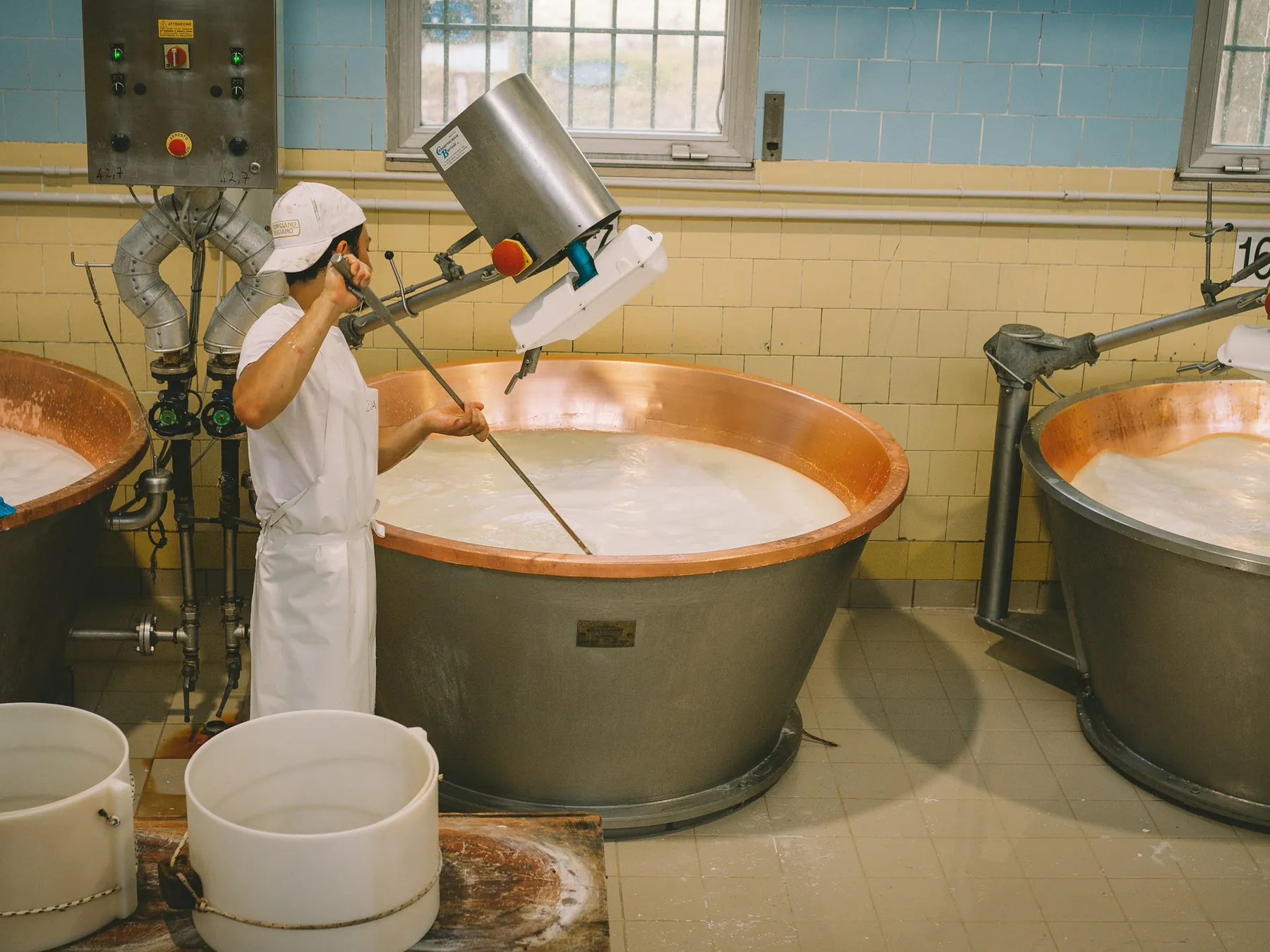 Cheesemaker stirring milk in large copper vats