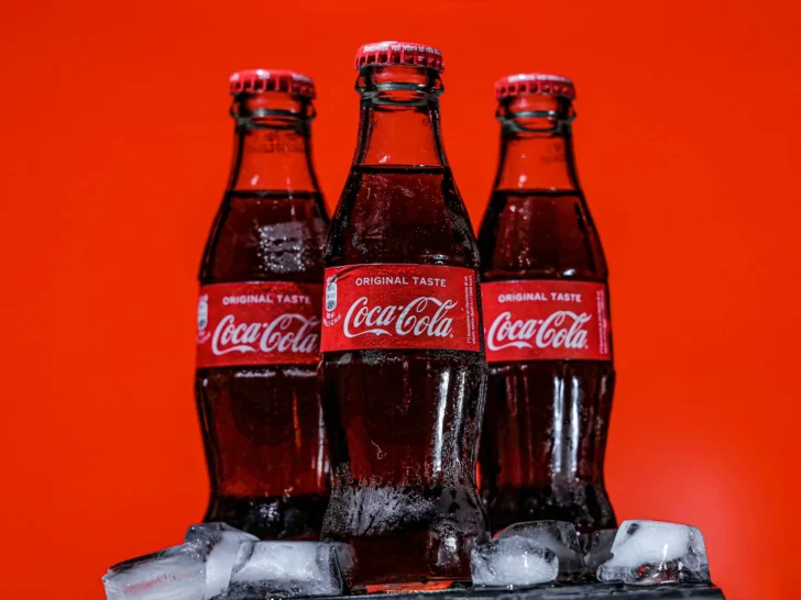 Three chilled Coca-Cola glass bottles against a red background