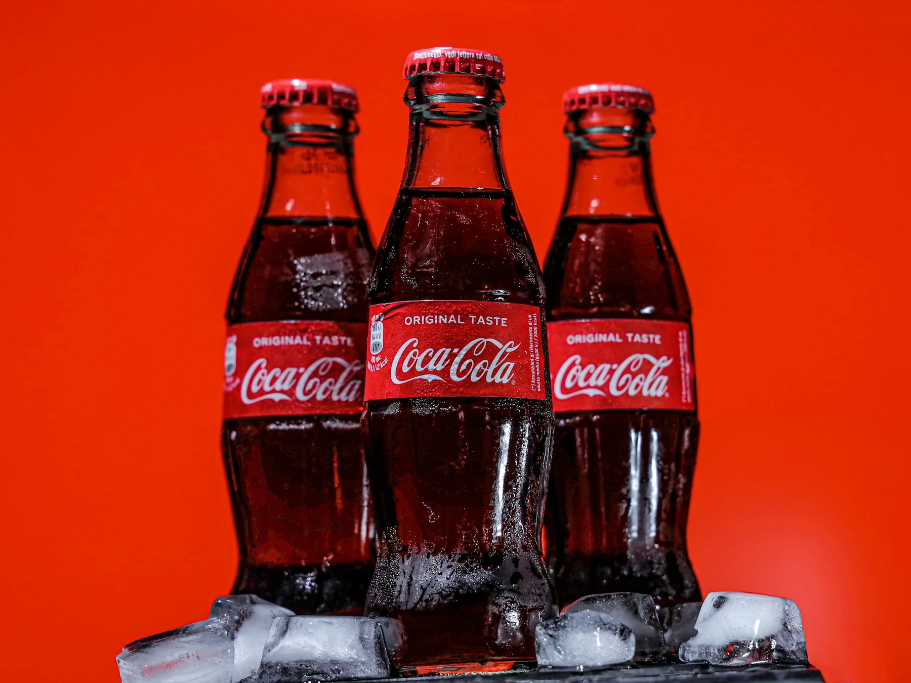 Three chilled Coca-Cola glass bottles against a red background