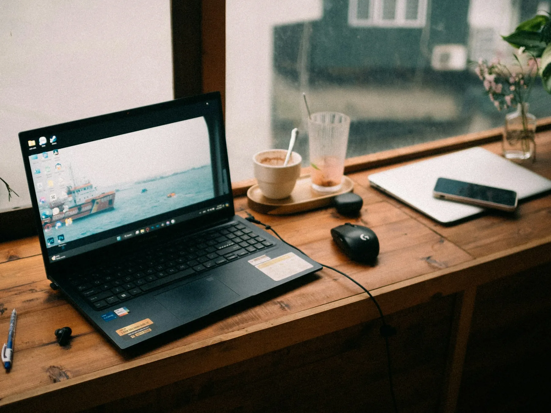 Open laptop computer on a wooden desk beside a mouse, phone, and drinks