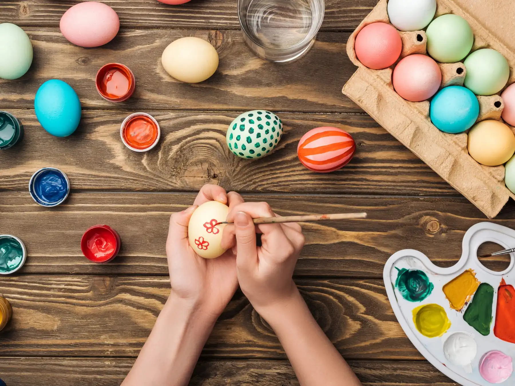 Hands painting colorful patterns on Easter eggs at a wooden table