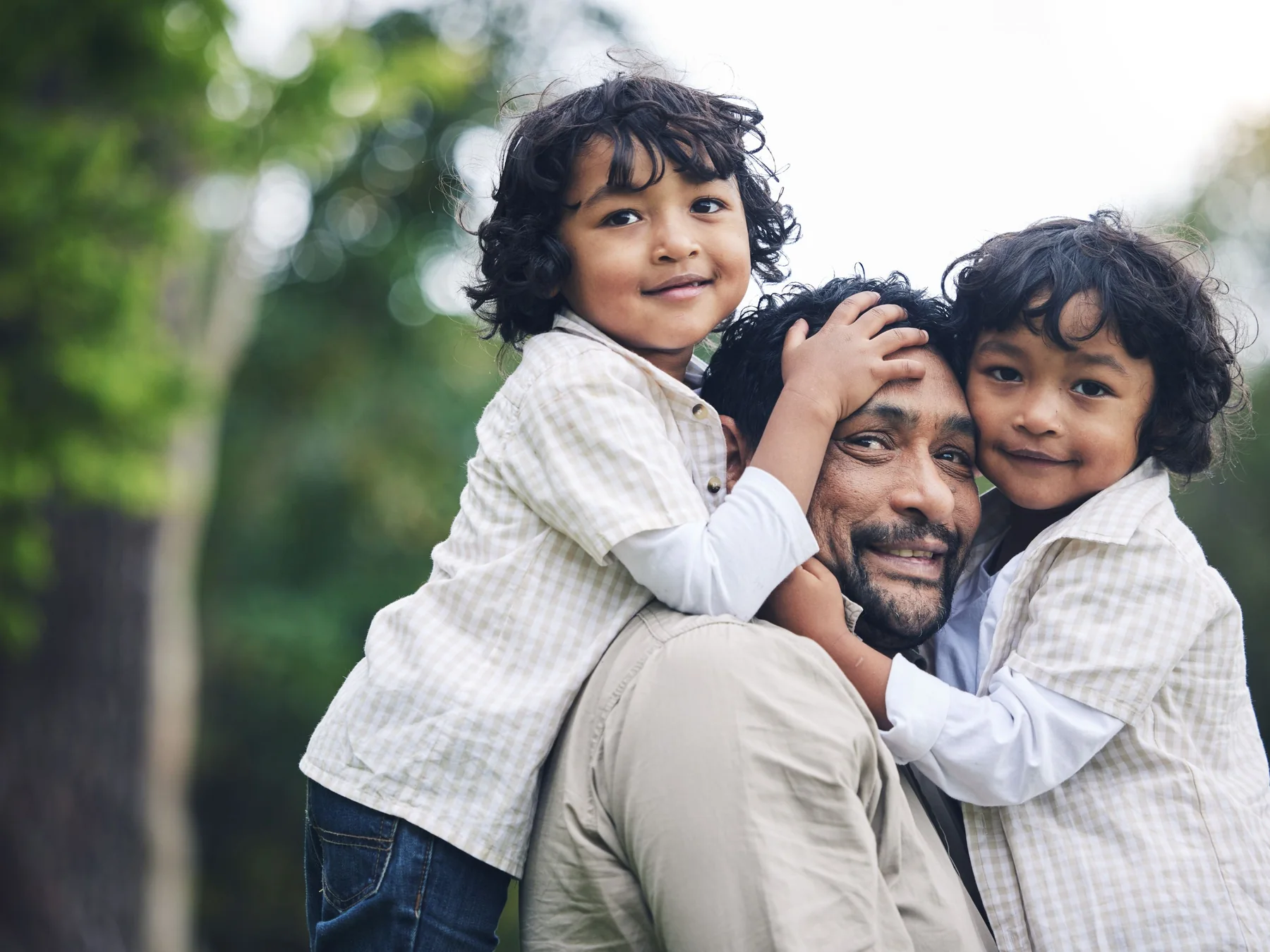 Father carrying two smiling children outdoors