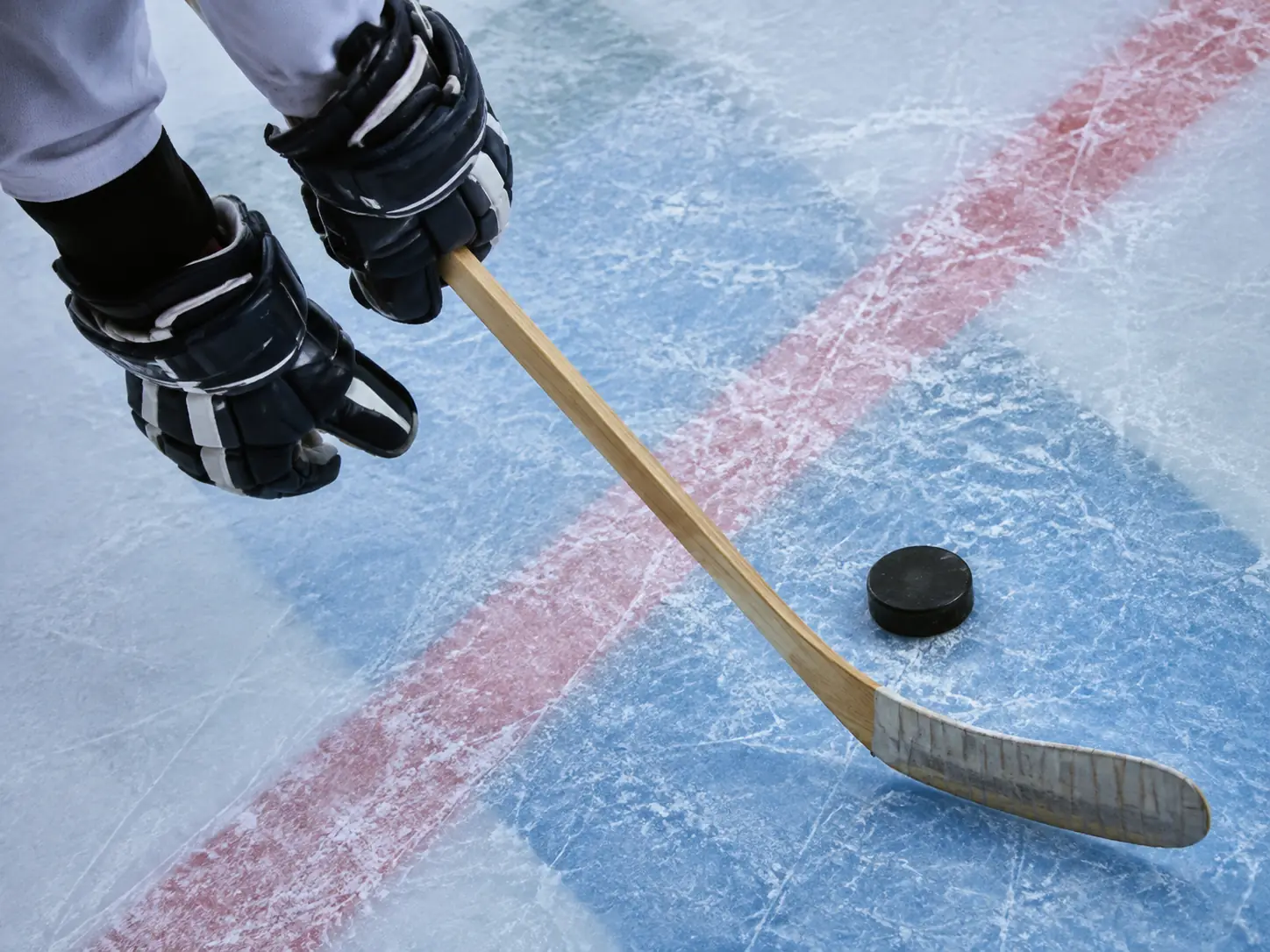 Gloved hockey player controlling a puck with a wooden stick on marked ice