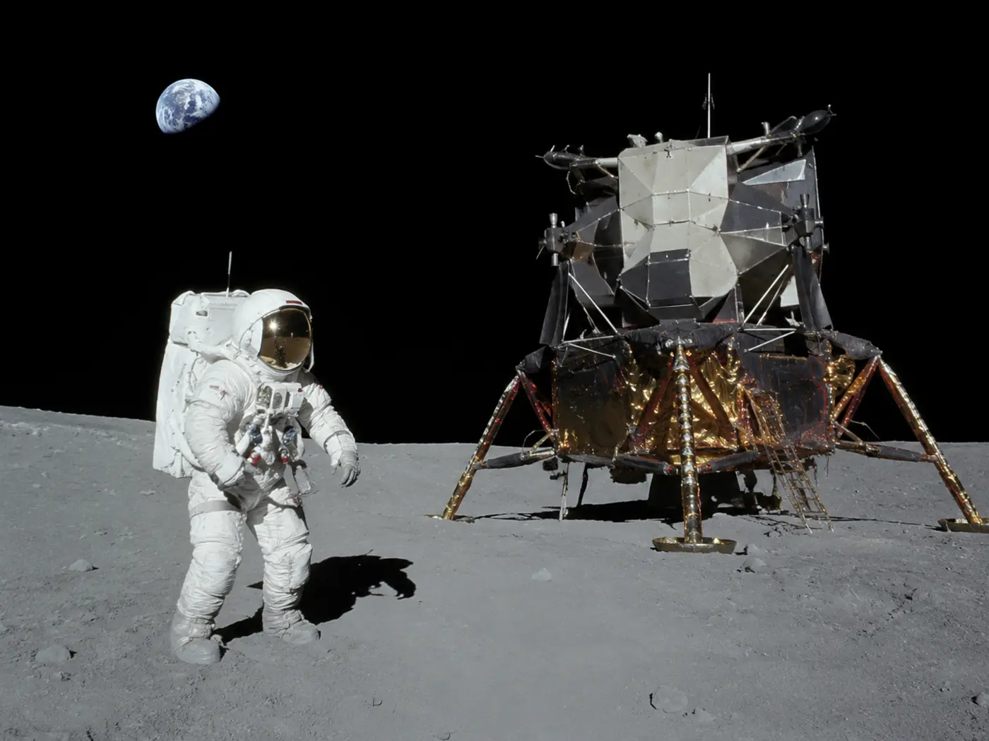 Apollo astronaut standing on the Moon beside a lunar module with Earth in the sky