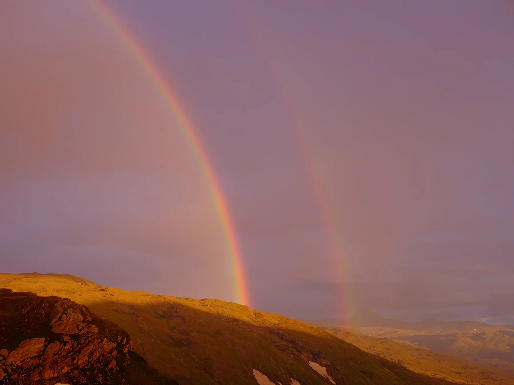Double rainbow above a mountain landscape at sunset