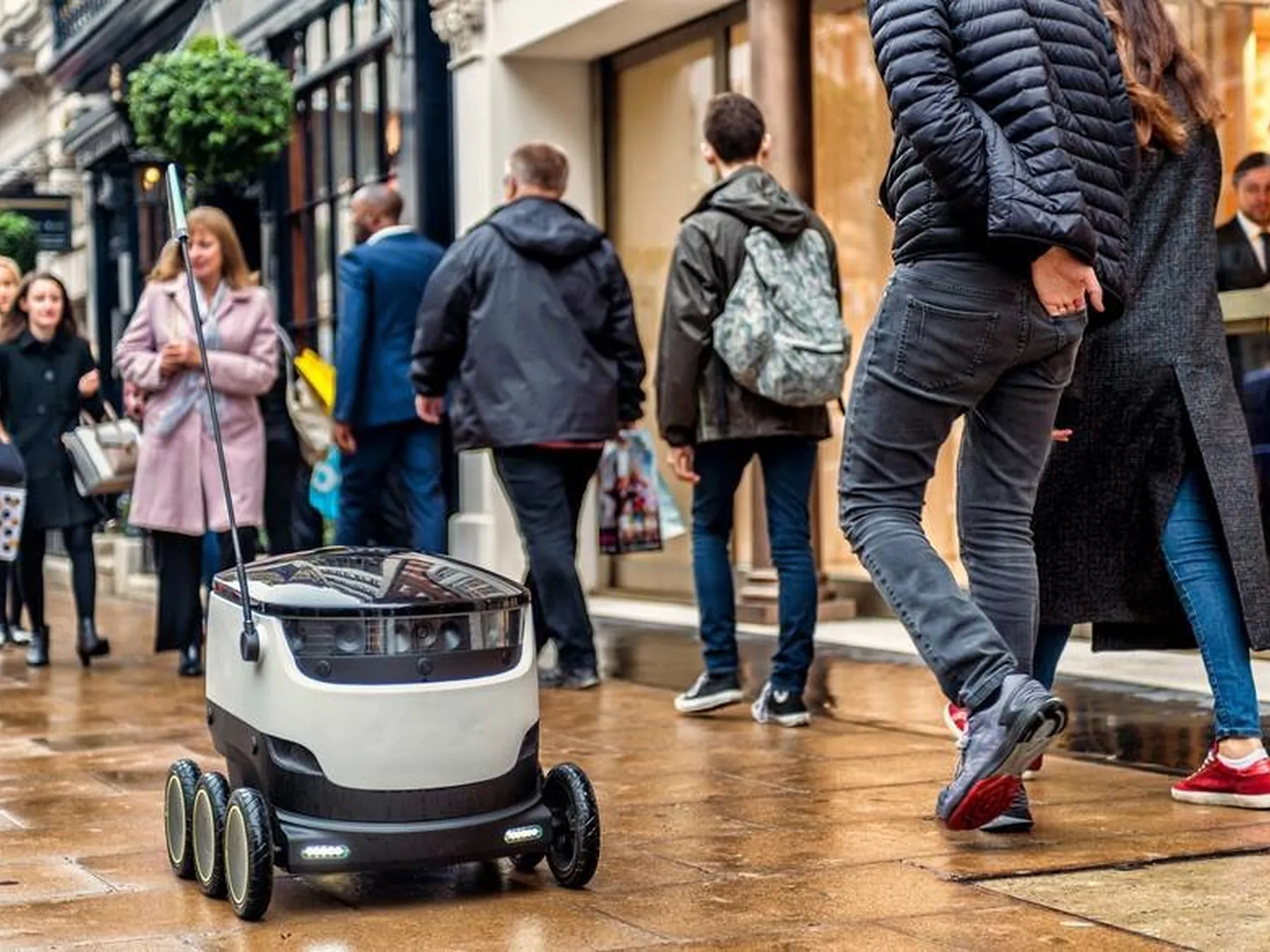 Six-wheeled autonomous delivery robot traveling along a city sidewalk