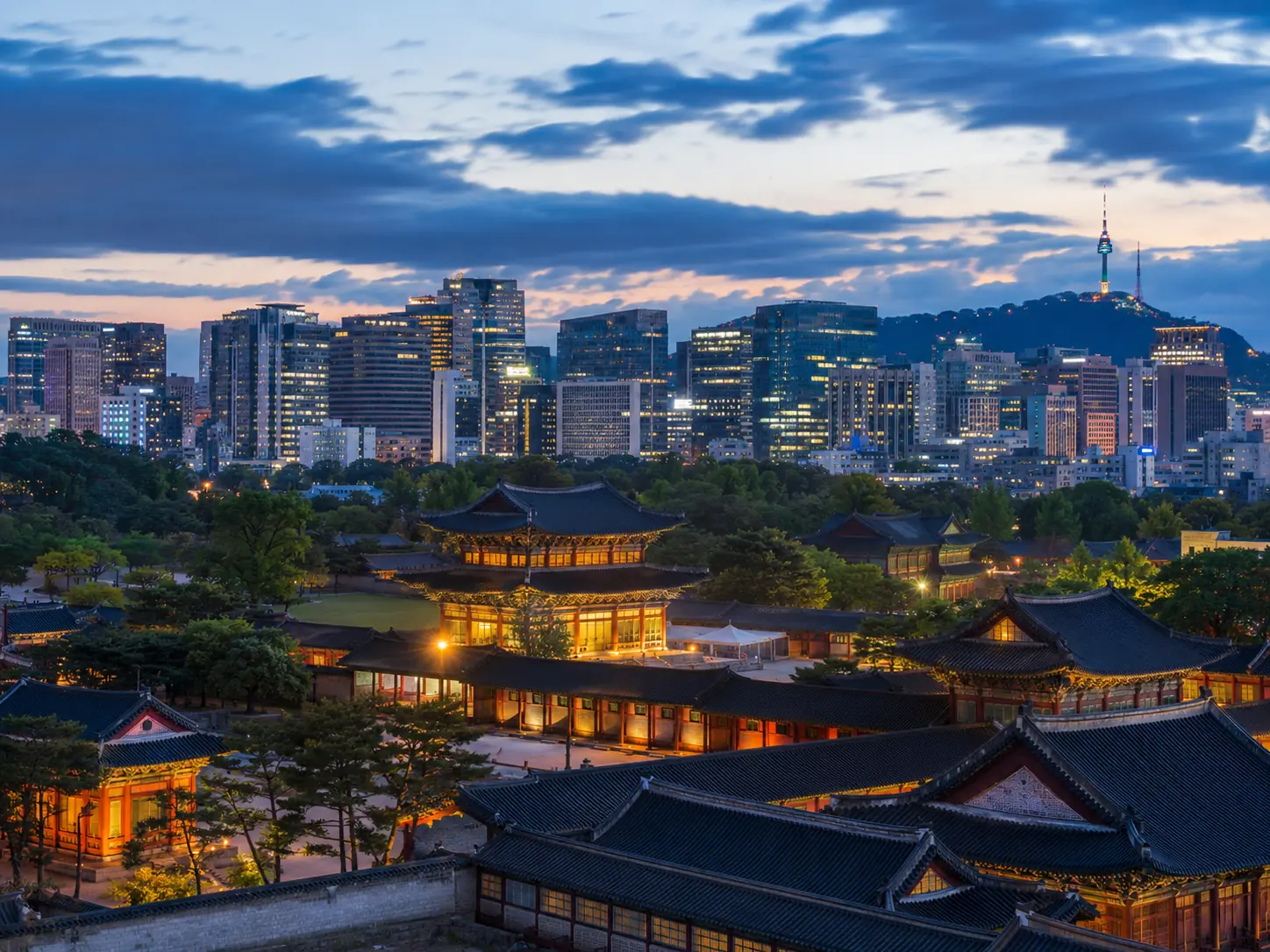 Seoul skyline at dusk with traditional Korean architecture in the foreground
