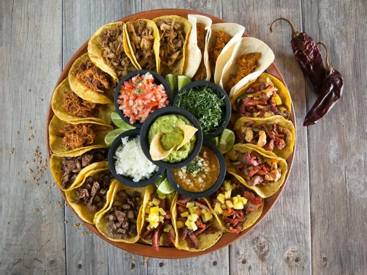 Large platter of assorted Mexican tacos with guacamole, salsa, onions, cilantro, and lime