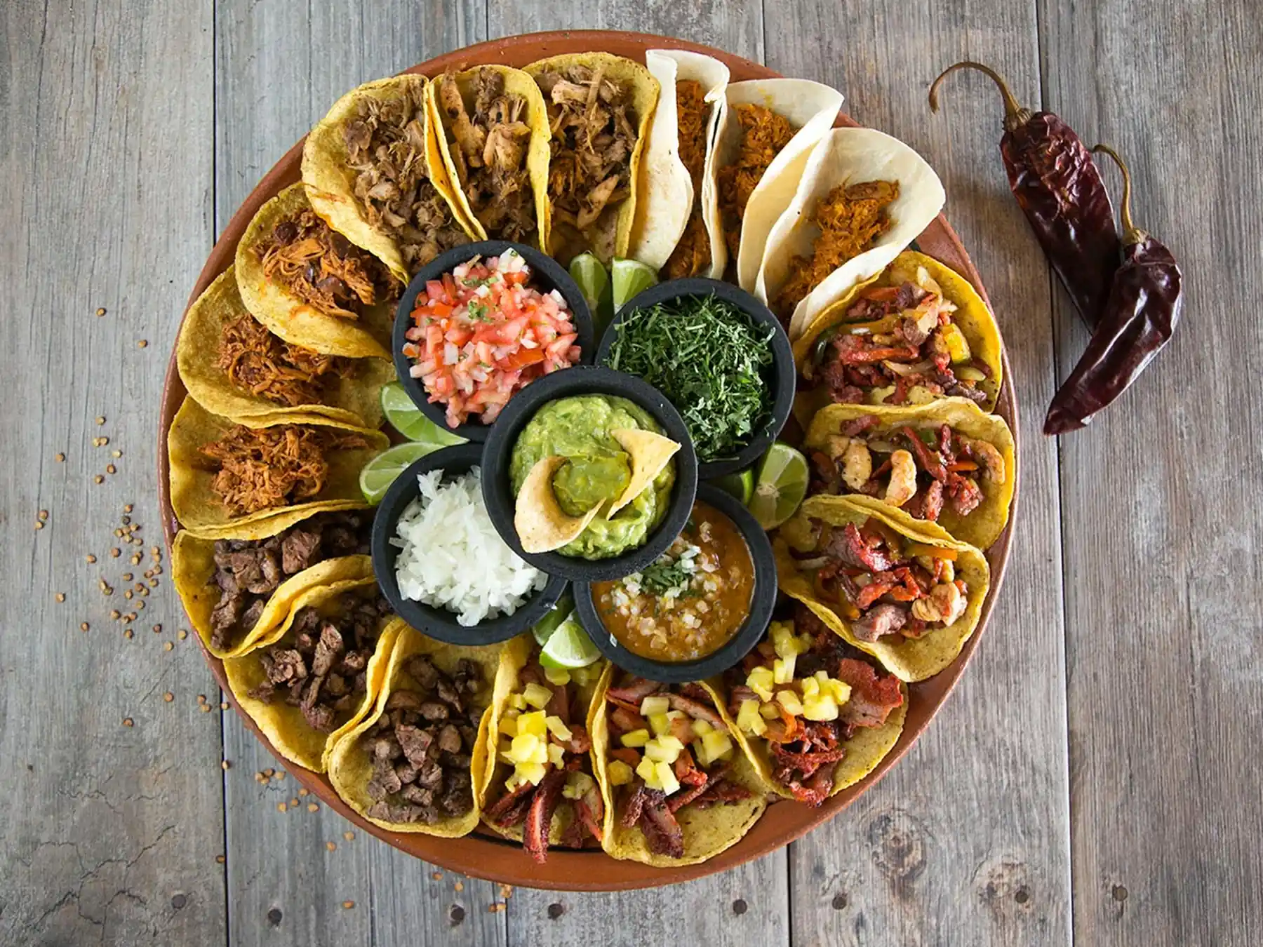 Large platter of assorted Mexican tacos with guacamole, salsa, onions, cilantro, and lime