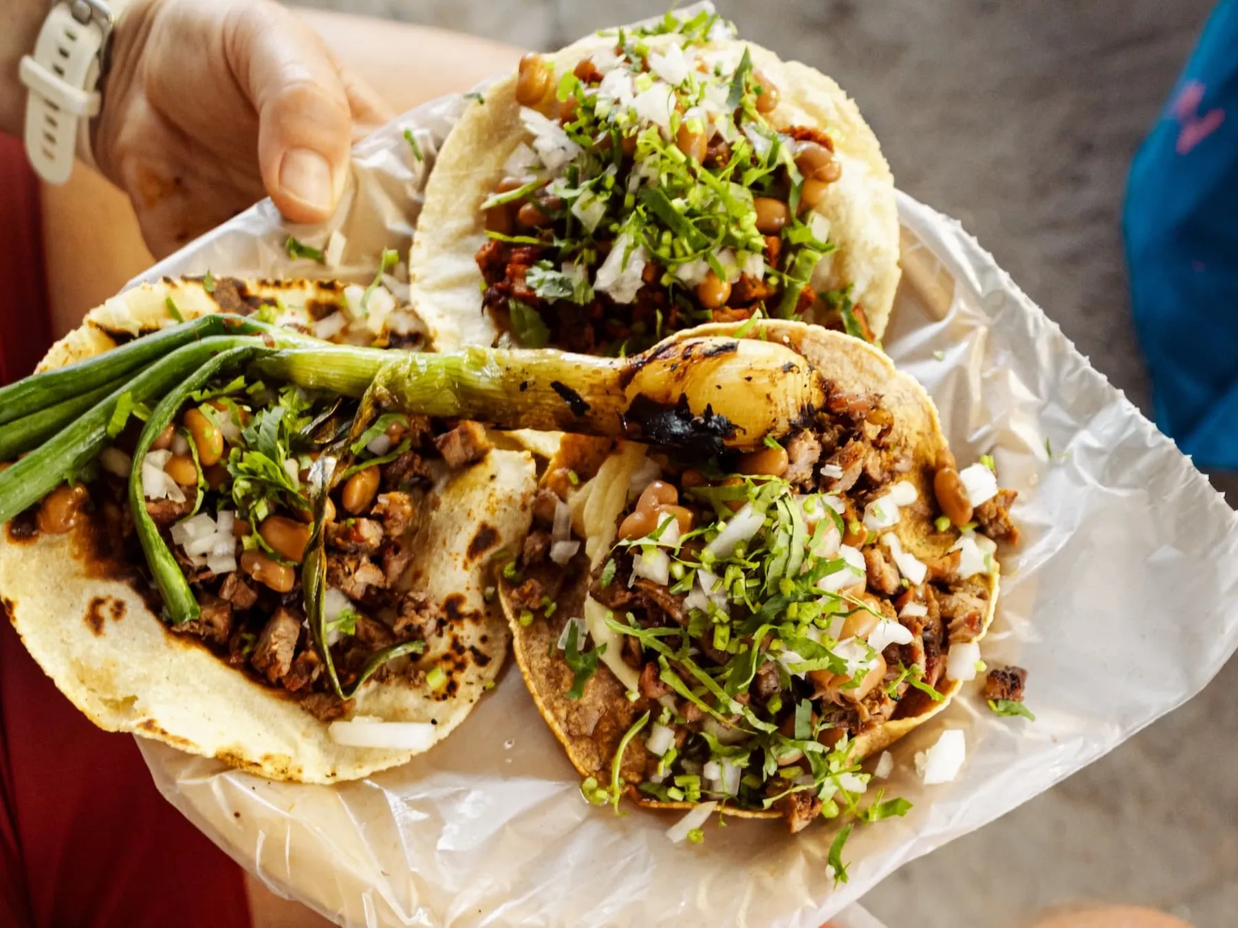 Three Mexican street tacos filled with grilled meat, beans, onion, and cilantro