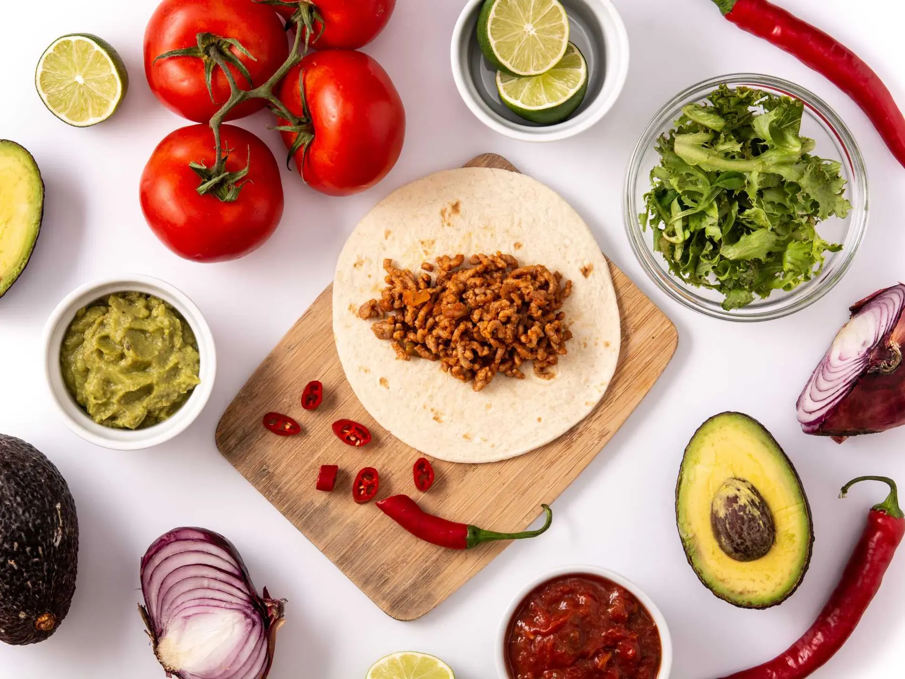 Overhead view of a taco being assembled with meat, avocado, tomato, lime, onion, and salsa