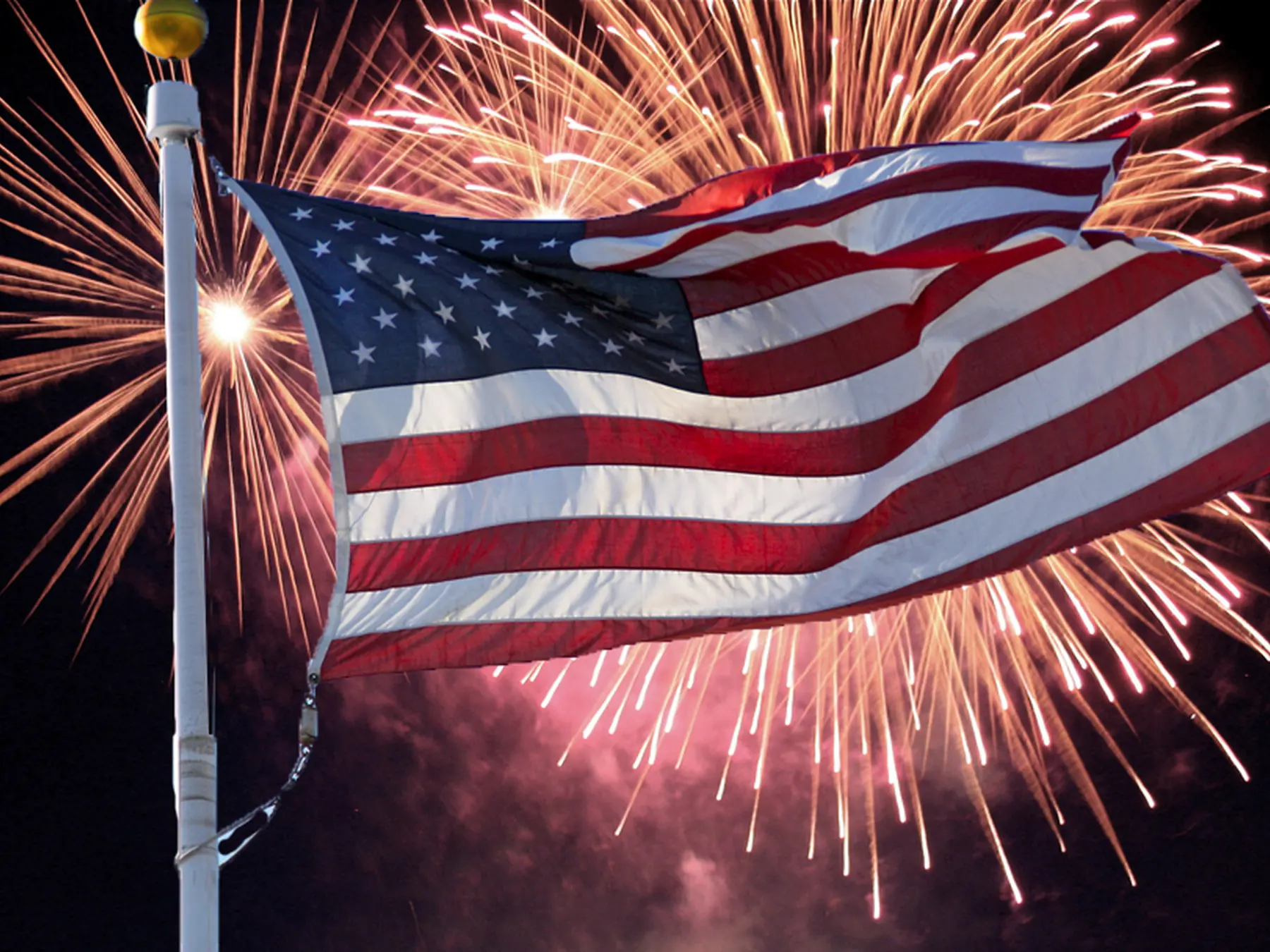 American flag waving in front of Fourth of July fireworks