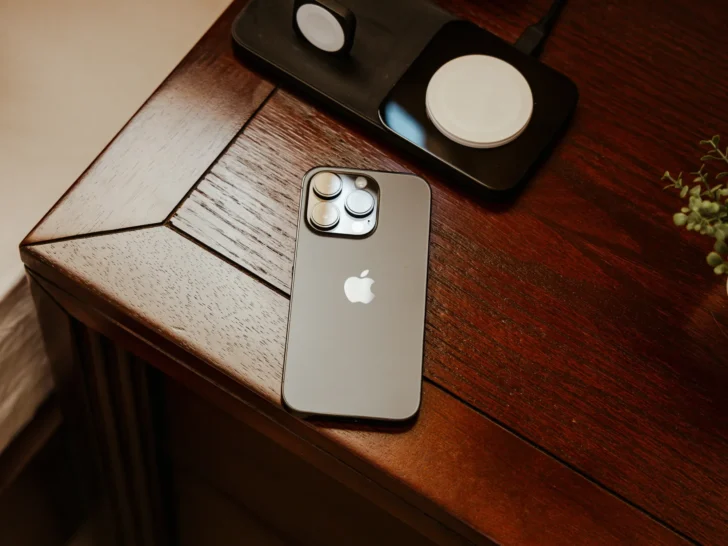 Modern Apple iPhone resting on a wooden table beside a wireless charger