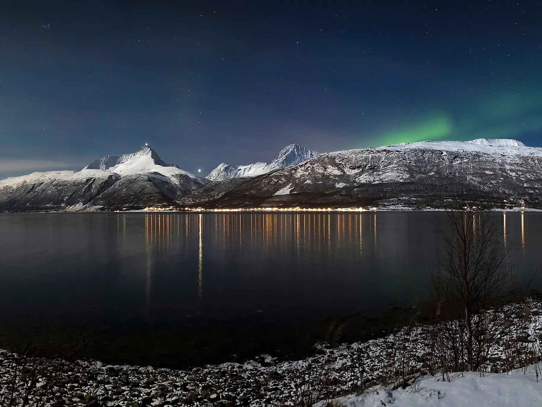 Green aurora borealis glowing across a dark sky above the water