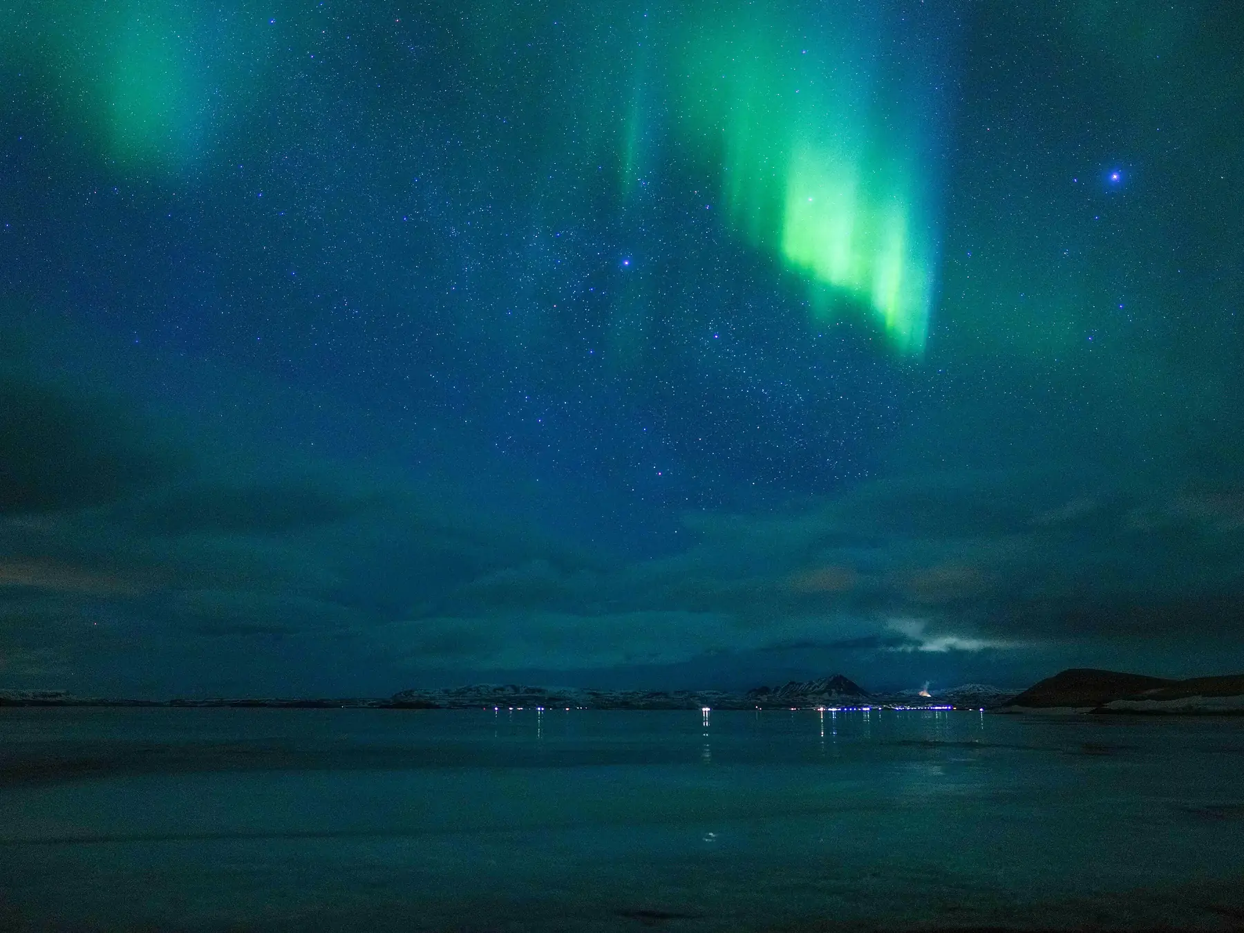 Green and purple northern lights above a snowy road and forest