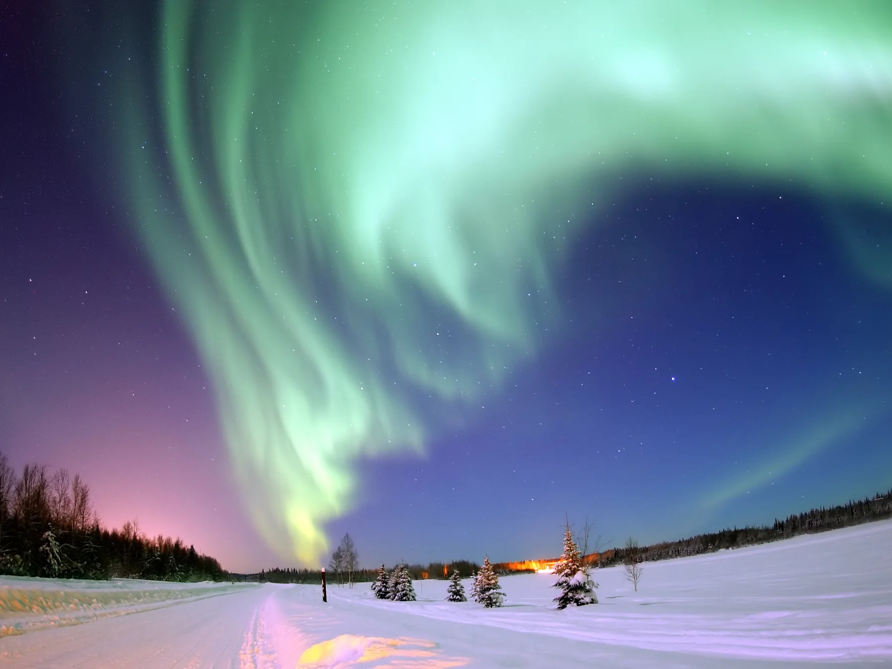 Green aurora borealis glowing above snowy mountains in Alaska