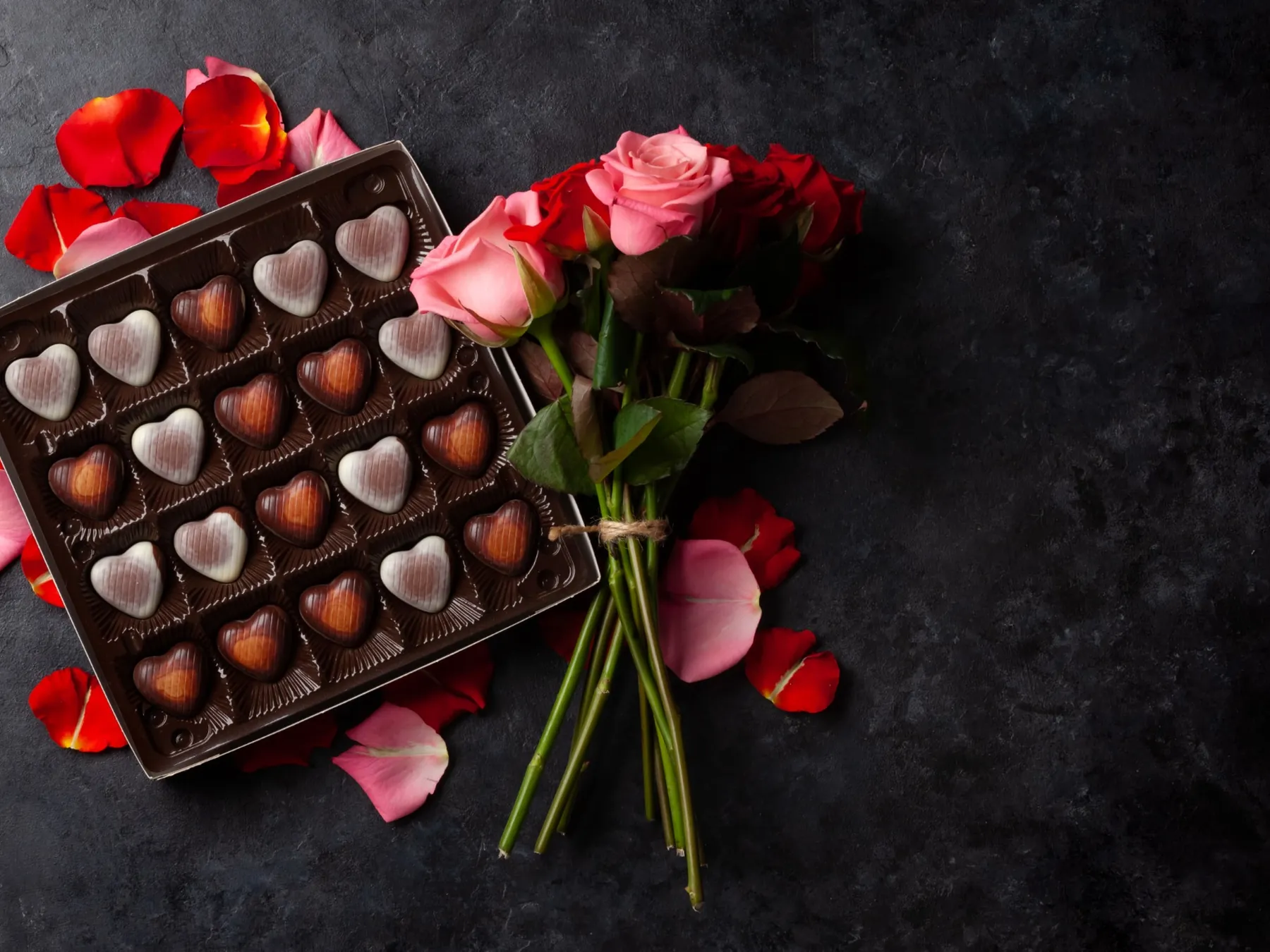 Heart-shaped chocolates arranged beside a bouquet of pink roses