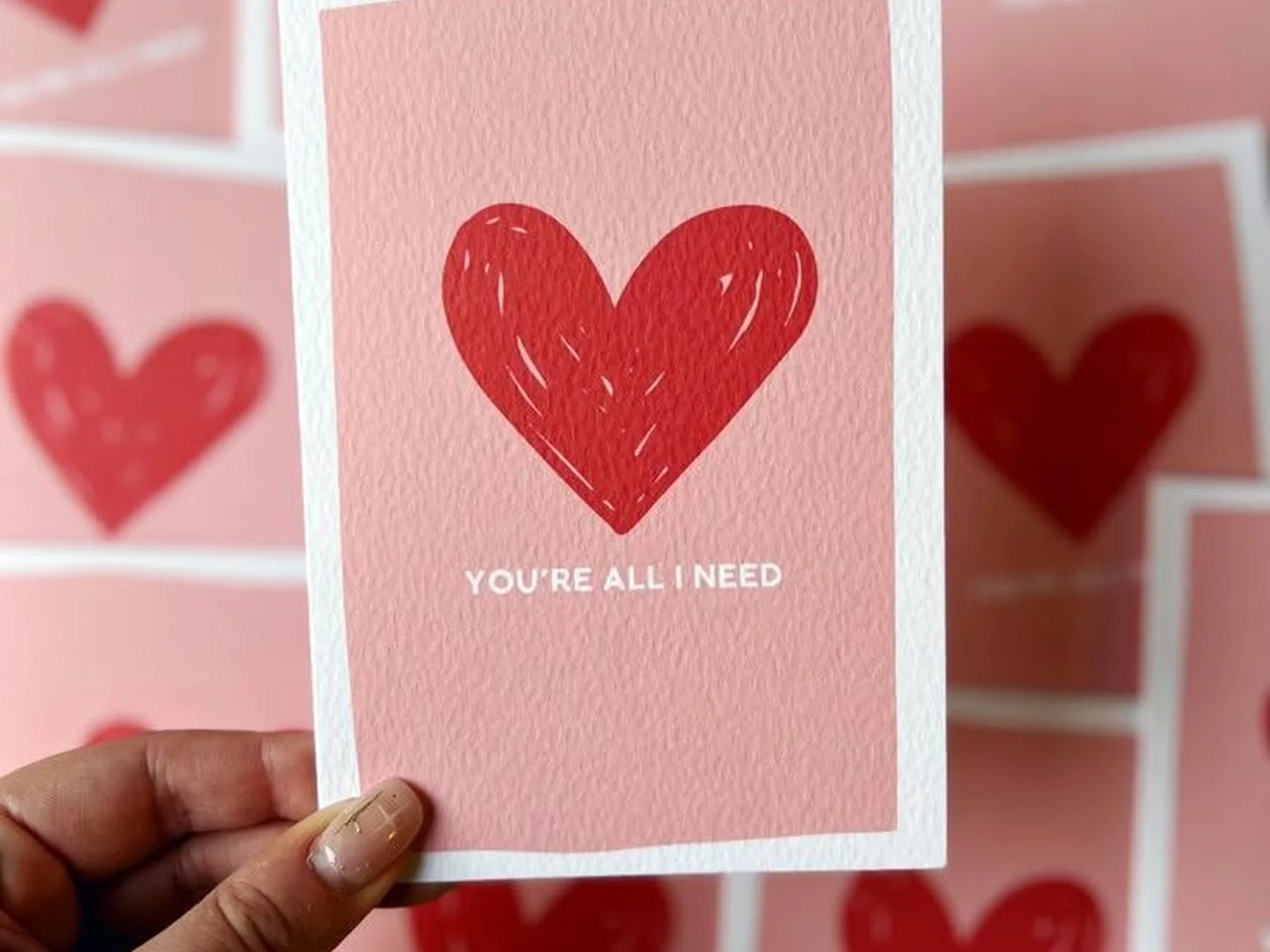 Hand holding a pink Valentine’s Day card decorated with a red heart