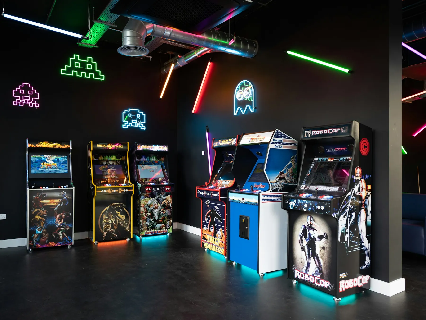 Row of classic arcade cabinets glowing beneath neon signs