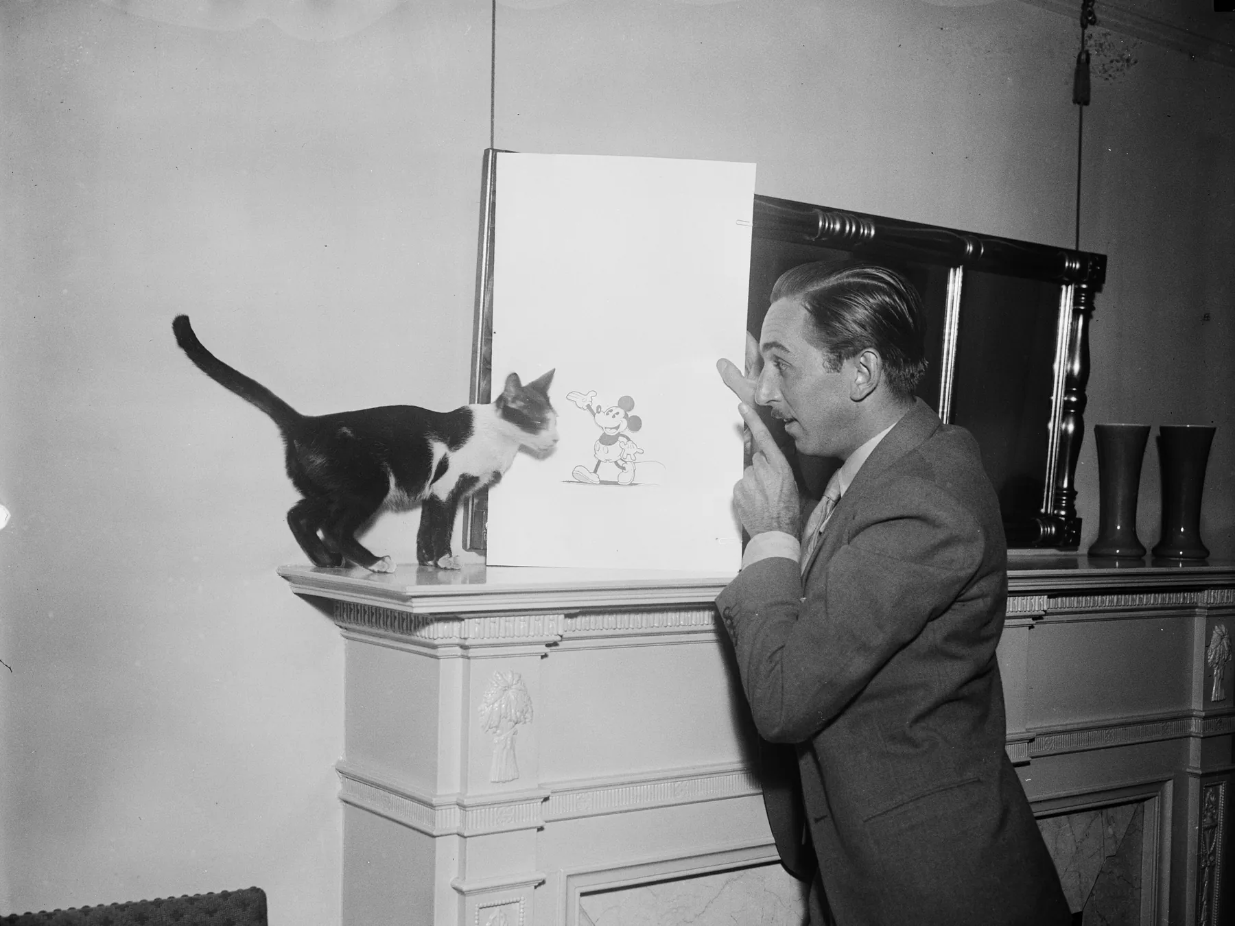 Walt Disney standing beside a drawing board and cat figurine