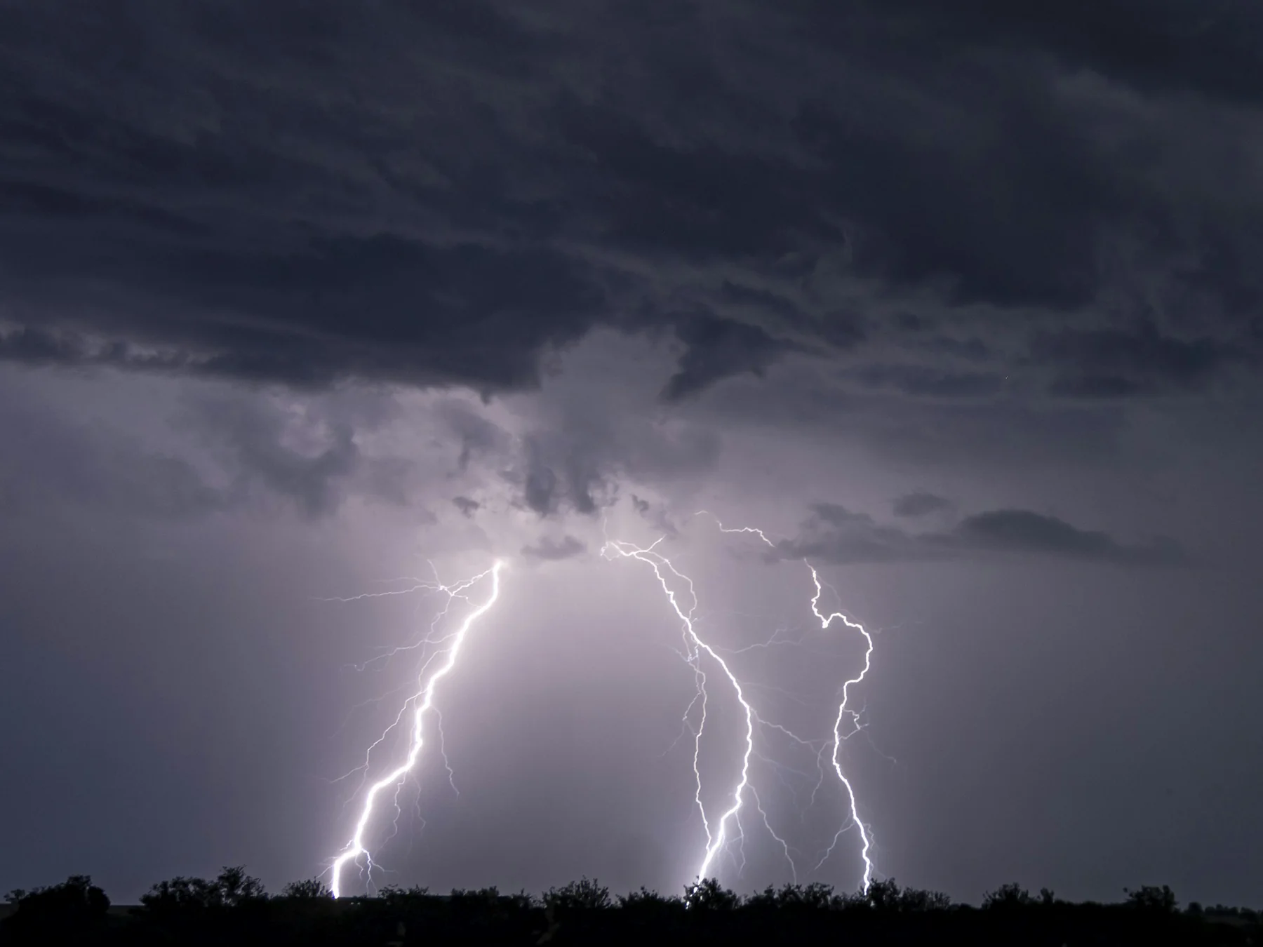 Lightning strikes beneath dark storm clouds over a distant horizon