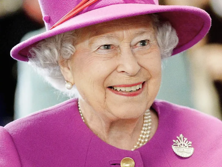 Queen Elizabeth II smiling while wearing a bright pink hat and coat