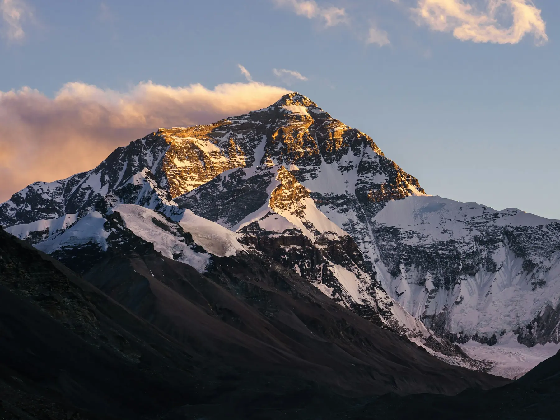 Sunlit Mount Everest glowing above dark mountain slopes